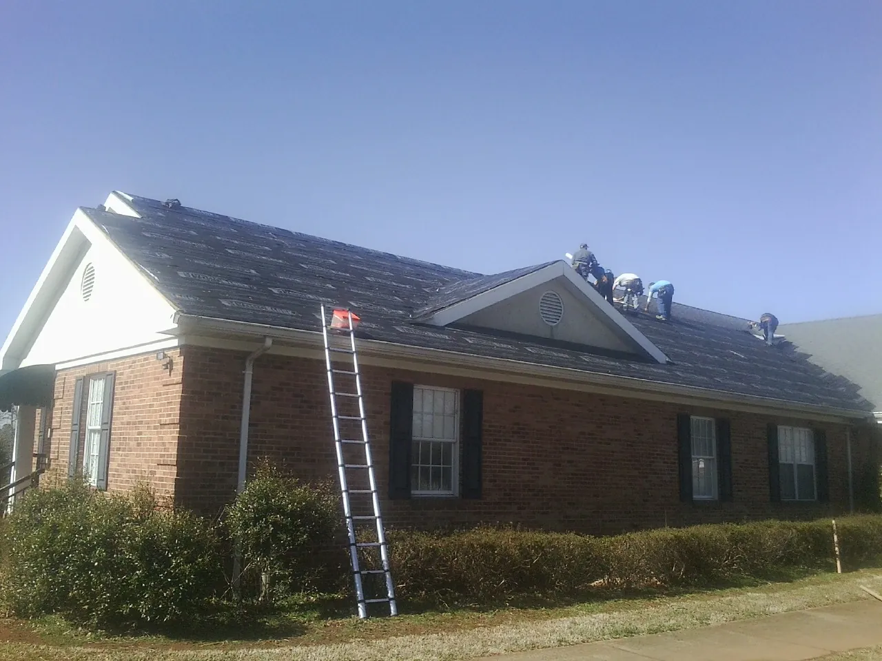 Crew tearing shingles off a brick ranch roof with a ladder set — Metal Roof Repair work by our crew in Joppa