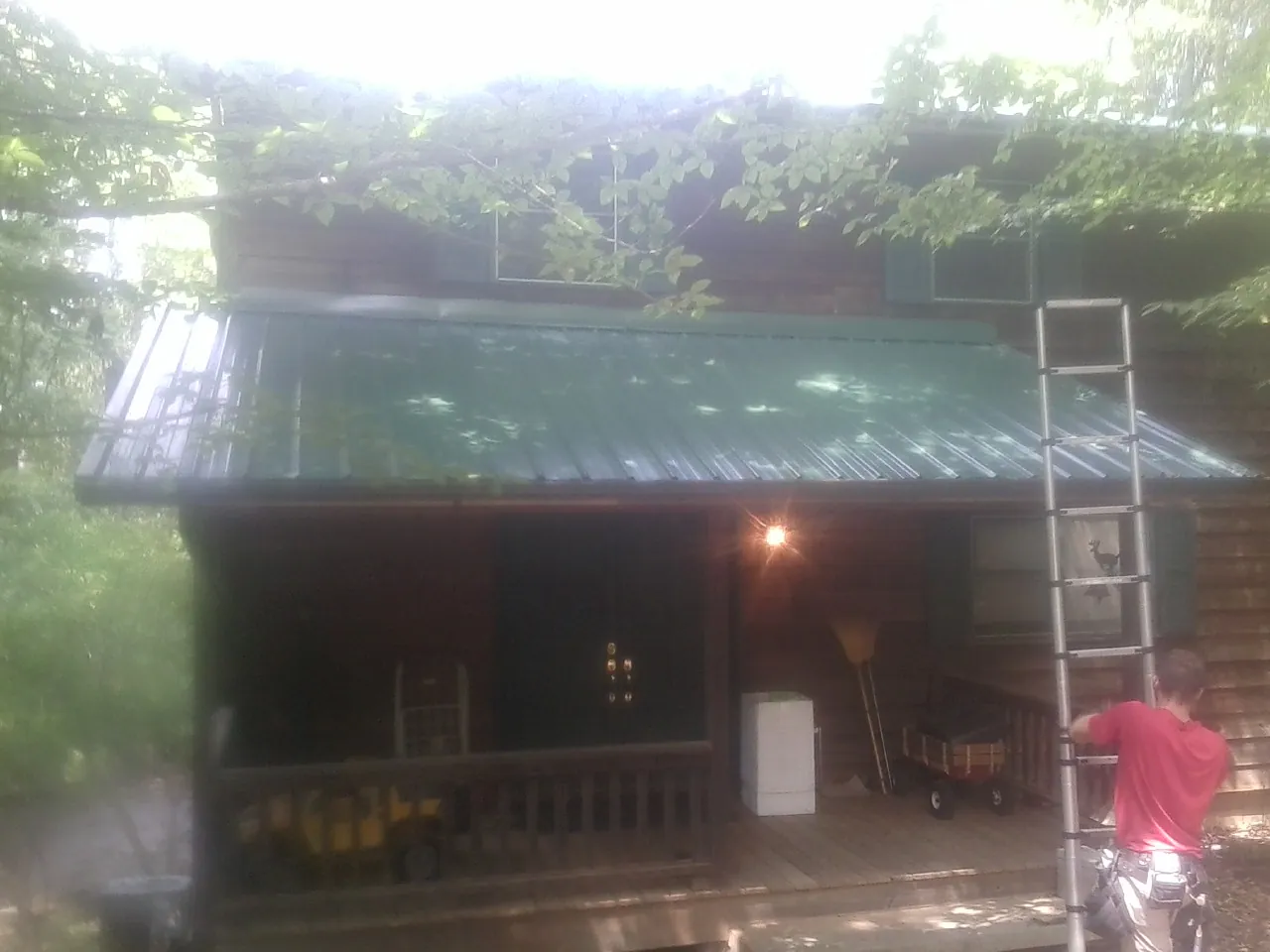 Worker on a ladder at the green porch roof of a wooded cabin in Joppa