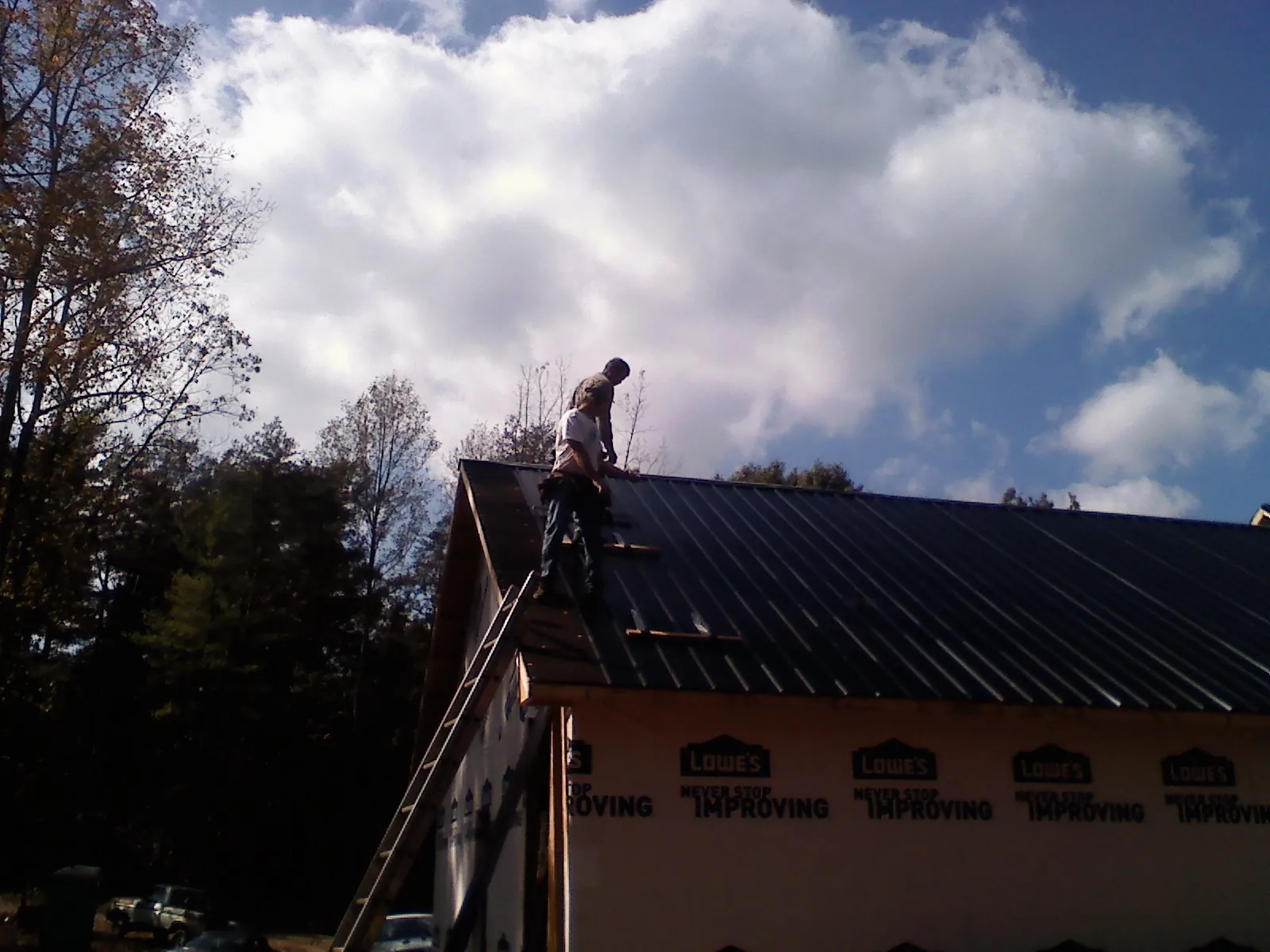 Roofer fastening dark metal panels high against a cloudy sky, from a Roof Inspection job in Joppa